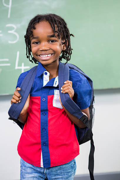 istock Smiling boy standing against board in classroom 590616946