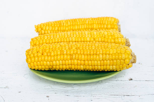 istock Bright yellow sweet corn on green plate on white background 590618700