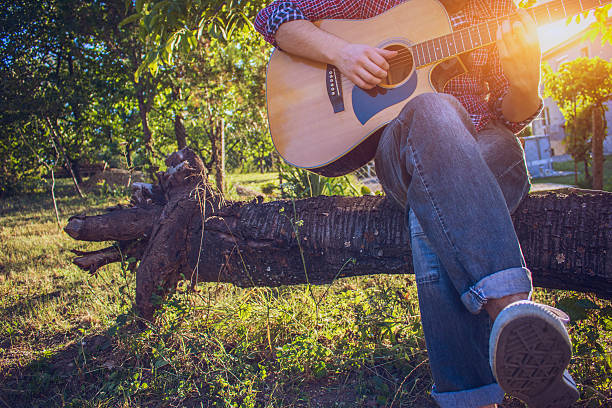 istock Hipster sitting on tree and playing acoustic guitar 590625096