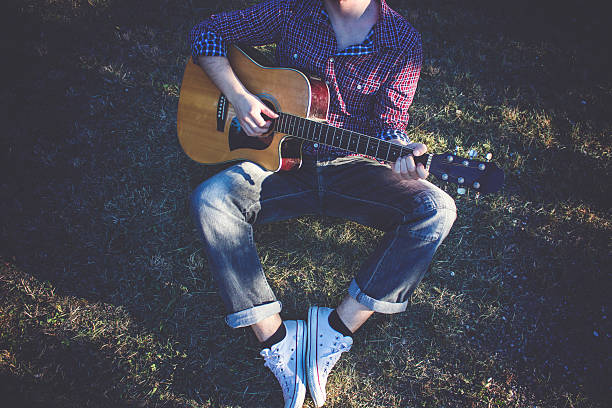 istock Boy sitting on grass and playing guitar 590625236