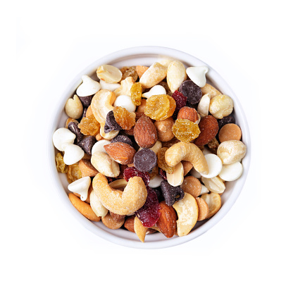 Small bowl of trail mix, including peanuts, almonts, cashews, dried cranberries, yellow raisins, chocolate chips, white chocolate chips, isolated on white