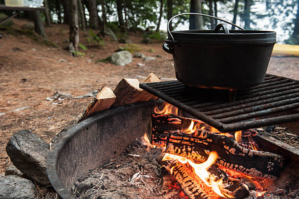 Juicy steaks sizzling on a metal grill over an open campfire in an outdoor setting. Rustic tools and earthy surroundings highlight the camping experience.