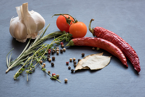 Dry red hot chili peppers, garlic, laurel leafs, tomatoes, seasoning, rosemary and savory on a dark background