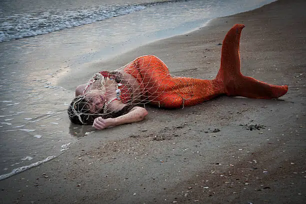 Mermaid in orange tail trapped in fishermen's netting is washed up on shore at the Atlantic Ocean, St. Augustine, FL, USA