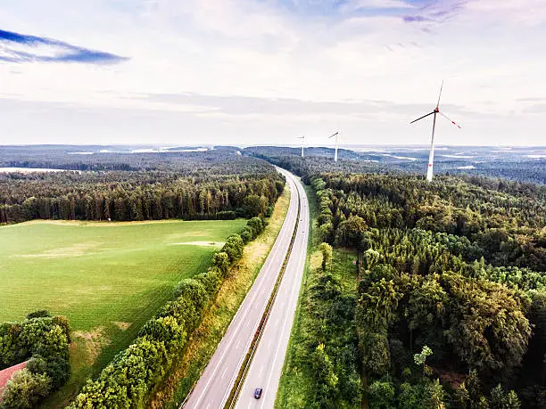 Photo of Highway in green forest, windmills, cloudy sky. Netherlands