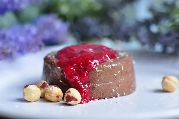 Vegan coconut chocolate pannacotta with raspberry sauce served with hazelnuts and grated coconut