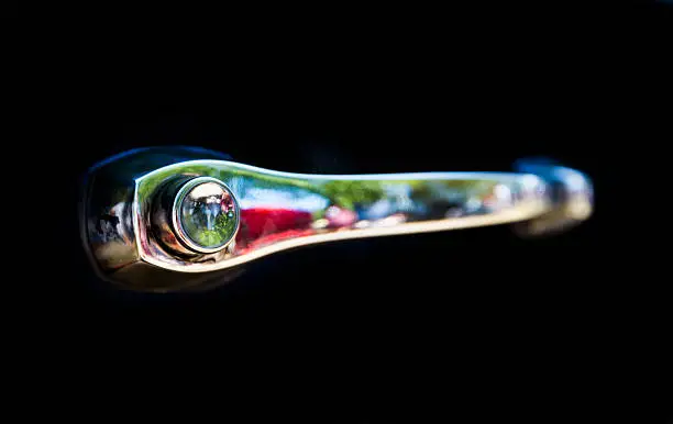 Detail of an attique car at a retro car parade. Retro car handle isolated on a black background.