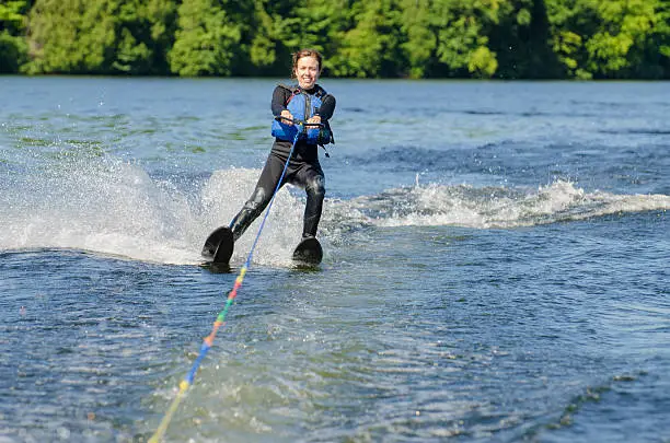 Woman in wet suit water skiing and smiling, in a lake, during a summer day