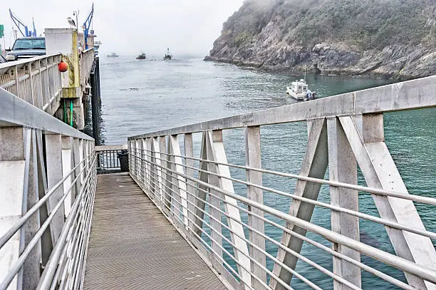 At the harbor in Trinidad California, many folks go on the fishing boats and try their luck in the ocean. This gangway allows the folks to board and debark the fishing boats at the water level below the pier. There are also more fishing boats in the harbor on this foggy day.