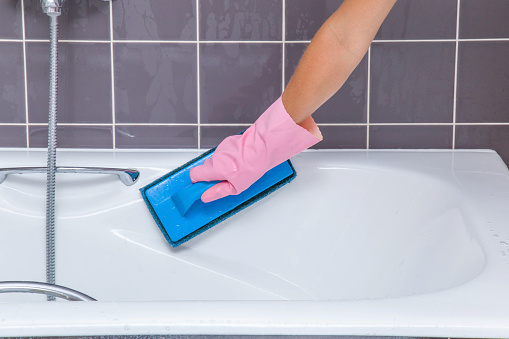 Hand in pink protective glove washing tiles and bath with professional cleaning pad. Early spring cleaning or regular clean up. Maid cleans house.