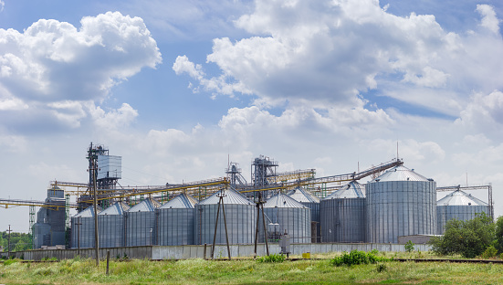 Grain storage system with corrugated steel storage bins and grain distribution system on the background of sky with clouds