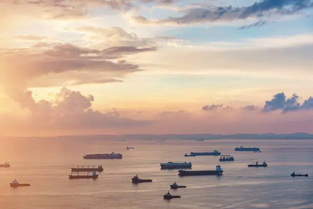 Aerial view of freight transportation ships, container ships and industrial boats at beautiful sunrise twilight light to the horizon close to singapore city transportation hub harbor. Singapore Strait, Singapore, Asia.