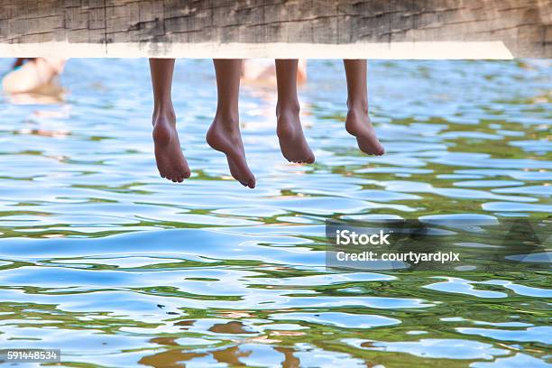 Boys Legs Dangling Down From Wooden Pier Over Water Stock Photo - Download Image Now