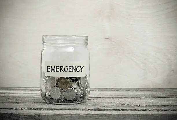 Label on a glass jar with the inscription - emergency. Glass jar with coins. Financial concept on wooden background