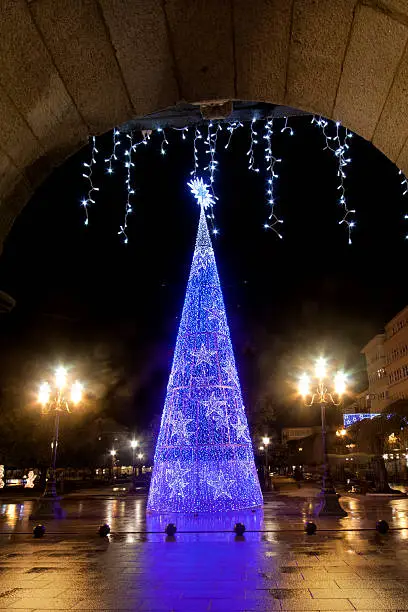 Modern lighting Christmas tree in a townsquare in Lugo, Galicia, Spain with stone arch upper frame.