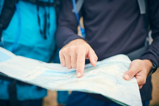 Midsection of travelers reading map. Selective focus is on man's hand searching for direction. Couple are hiking on vacation.