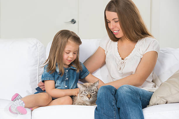 istock Mother and daughter sitting on sofa and cuddling cat 591814408
