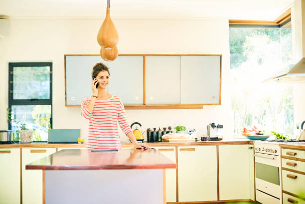 istock Happy woman talking on smart phone in kitchen 591815114