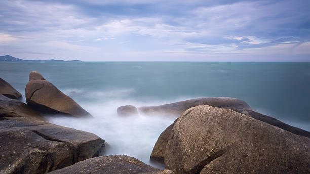 istock Long exposure seascape with foamy waves splashing against a rock 591815634