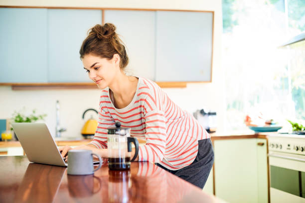 istock Woman using laptop by French press and mug in kitchen 591818018
