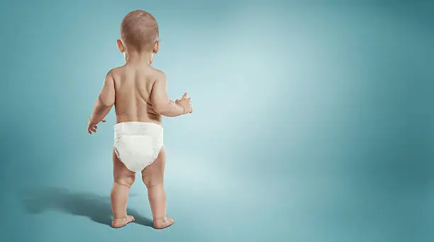 Photo of Infant child baby toddler standing in diapers. Back view