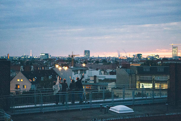 Berlin: small group of young adults standing on rooftop waving sparklers, Berlin skyline in background
