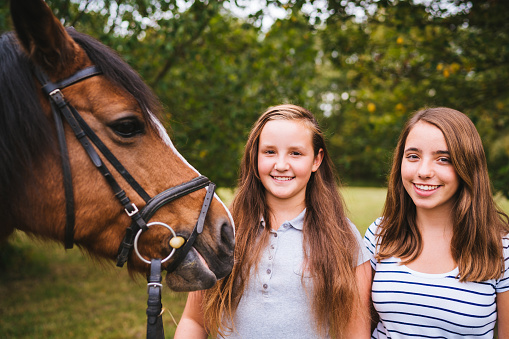 Young girls together after a horseback ride with their horse. Smiling together side by side with.