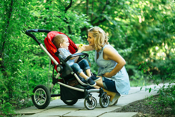 mujer embarazada con su hijo en cochecito - baby mother summer park fotografías e imágenes de stock