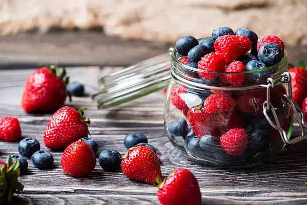 Berries in glass jar, over wooden background. Strawberries, Raspberries, Blueberry