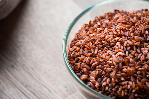 Organic brown rice in glass bowl over wooden background