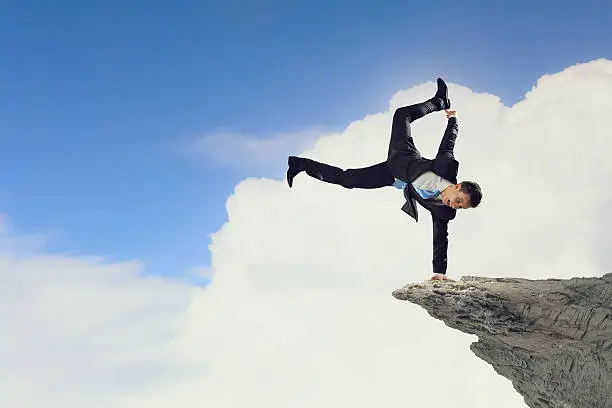 Active businessman making handstand on rock edge
