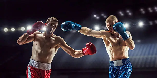 Two professional boxers fighting on arena in spotlights 