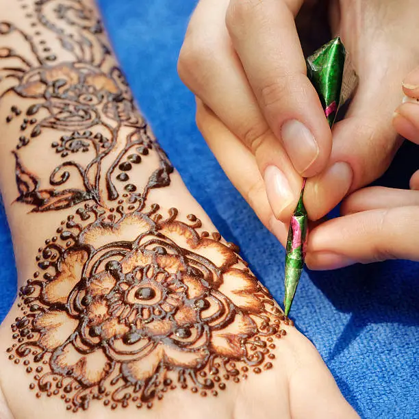 young woman mehendi artist painting floral ornament henna on the hand
