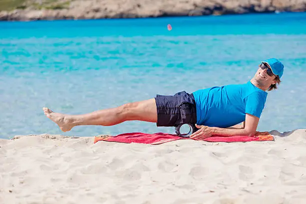 A male guy, doing some exercises with a black roll at the beach. XXXL size image. Image taken with Canon EOS 5Ds and EF 70-200mm USM L 2,8. 