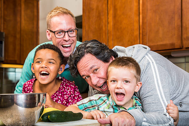 Laughing Family with Gay Dads in Kitchen Same sex couple and kids having fun at meal time gay daddy stock pictures, royalty-free photos & images
