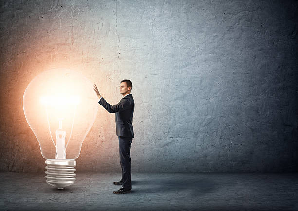istock Businessman stands touching big glowing light bulb 591842770