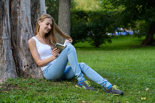 istock Young woman reading a book in the park 591844420