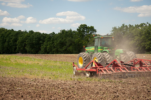 Grabill, Indiana - June 13th, 2011: John Deere green tractor tilling the ground to prepare for summer planting of hay, corn, and soybeans in Indiana, USA. Driving through the field with a disk tiller. 
