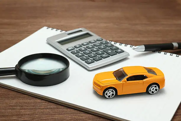 Photo of Toy car, magnifying glass, calculator, pen and notebook.