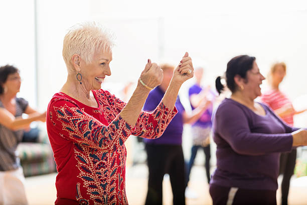 Senior woman enjoys dance class Beautiful senior woman snaps her fingers as she learns new dance moves during dance class at her senior center. People are dancing in the background. dance studio instructor stock pictures, royalty-free photos & images