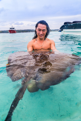 Young asian man holding stingray in the water.