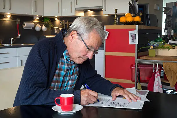 Elderly man (myself) in his open kitchen solving a puzzle with coffeecup next to him. He does that almost every morning.