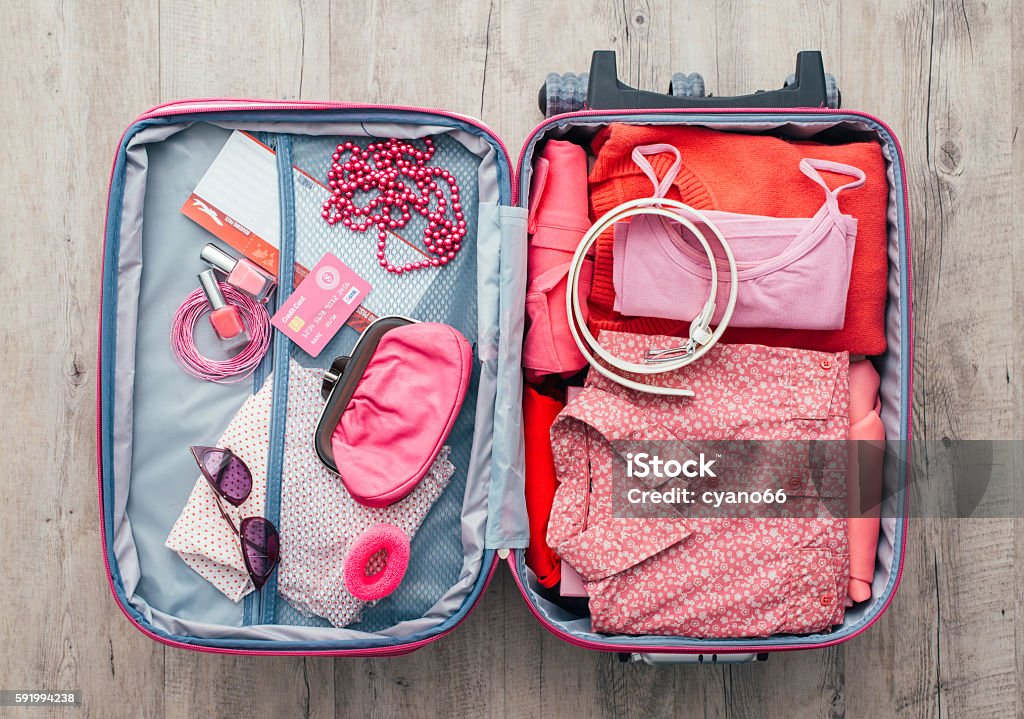 Woman getting ready to leave Woman's open bag on a desktop with clothing and accessories, she is packing and getting ready to leave, travel and vacations concept Suitcase Stock Photo