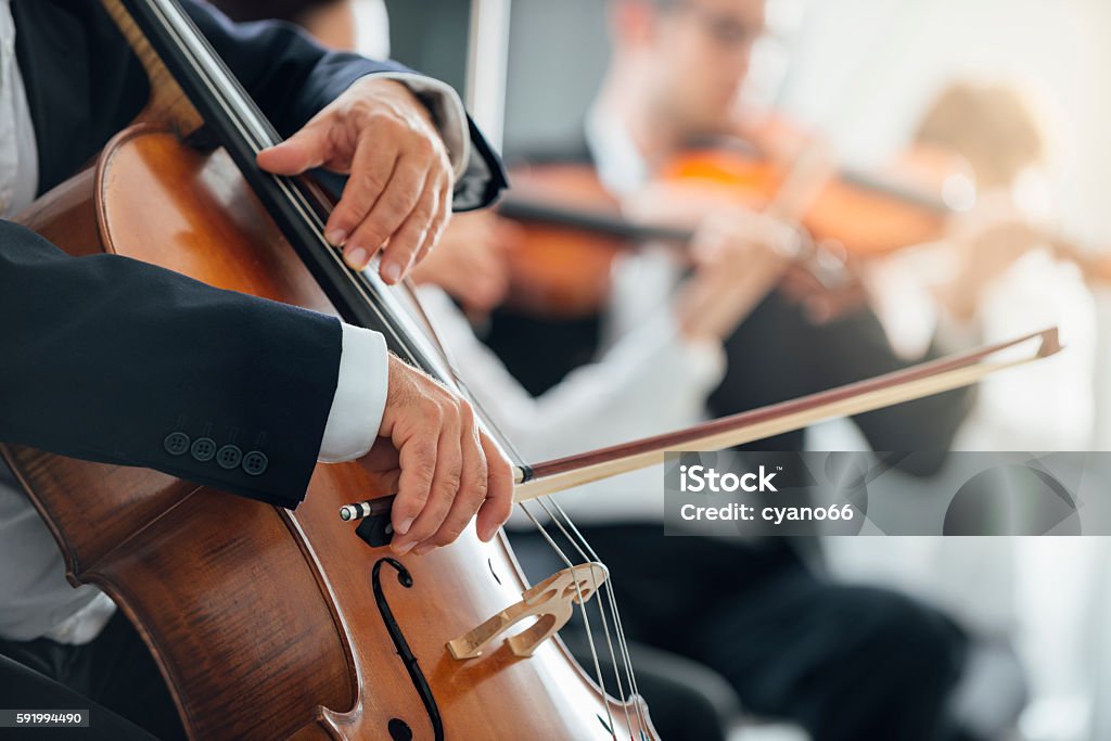 Symphony orchestra performance, string section String section of classical music symphony orchestra performing, cellist playing on foreground, hands close up Orchestra Stock Photo