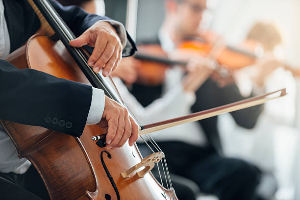 Symphony orchestra performance, string section String section of classical music symphony orchestra performing, cellist playing on foreground, hands close up symphony orchestra photos stock pictures, royalty-free photos & images