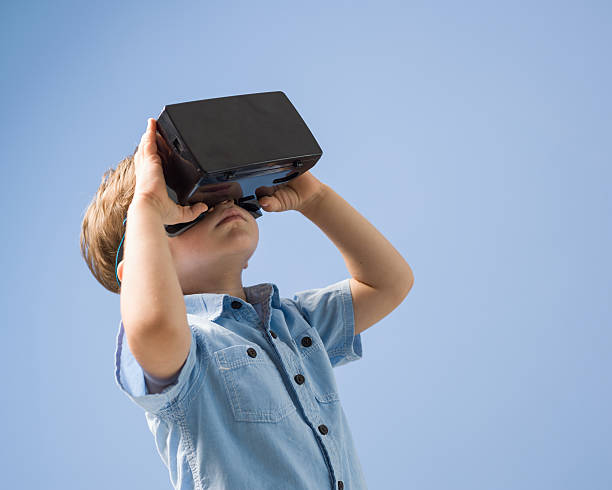 istock Little Boy Watching Through VR Glasses On Blue Background 592004172