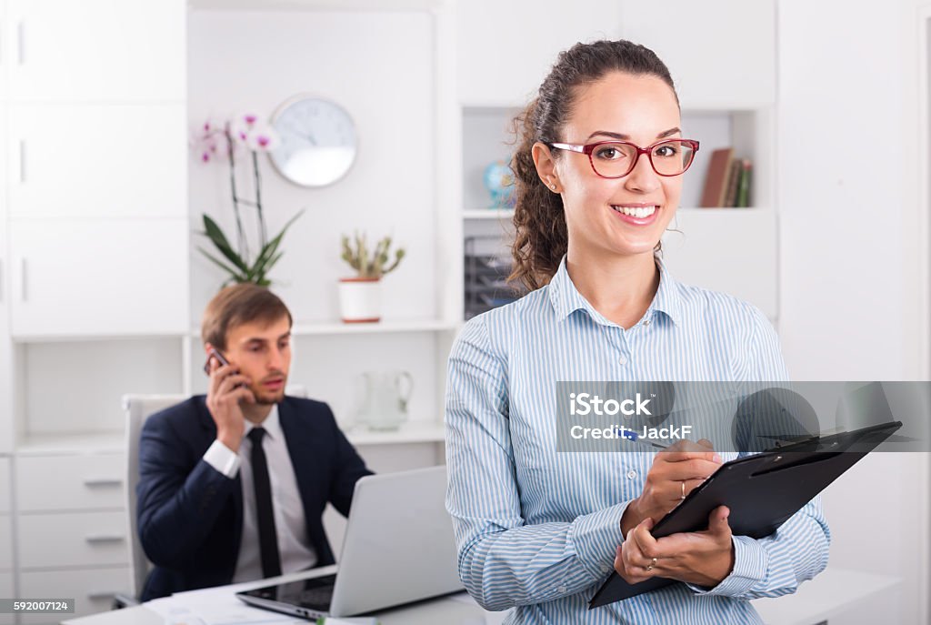 cheerful young woman manager holding cardboard in office cheerful young woman manager holding cardboard and smiling in office Secretary Stock Photo