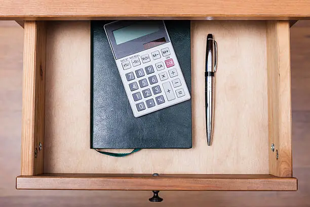 above view of ballpen, calculator and notebook in open drawer of nightstand