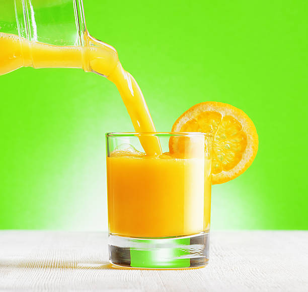 istock Orange juice pouring from jug into a glass 592031450