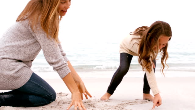 Mother and daughter drawing in the sand